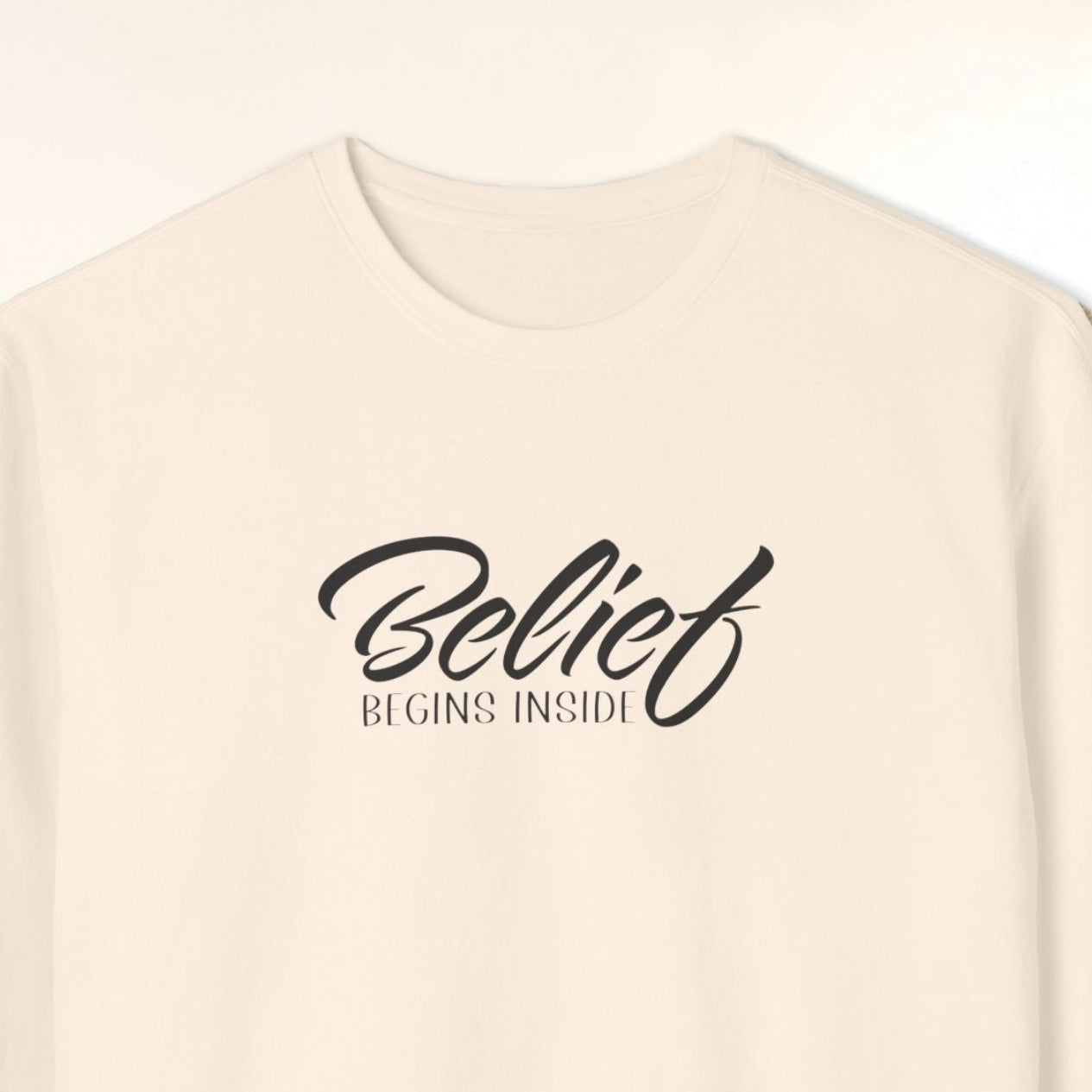 White sweatshirt with 'Belief Begins Inside' text on a nature background